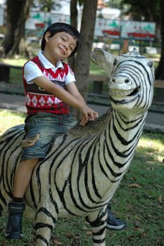 little asian boy sit down on zeebra statue in park
