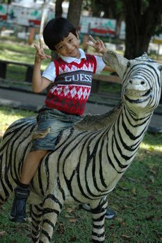 little asian boy sit down on zeebra statue in park
