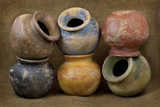 six small plant clay pots (mass produced planters) with rough color finish on dark burlap texture background, still life