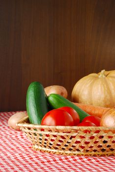 Autumn vegetables mix including onion, carrot, tomatoes, potatoes, cucumbers and pumpkin on red-white tablecloth