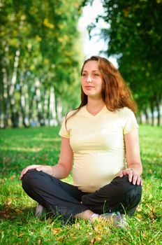 Beautiful pregnant woman relaxing on the grass in the park