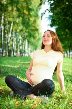 Beautiful pregnant woman relaxing on the grass in the park