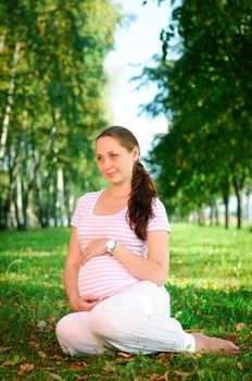 Beautiful pregnant woman relaxing on the grass in the park