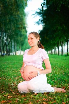 Beautiful pregnant woman relaxing on the grass in the park