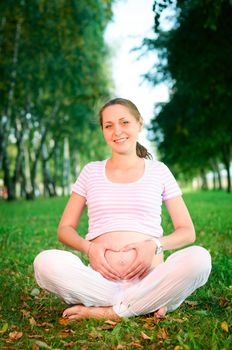 Beautiful pregnant woman relaxing on the grass in the park