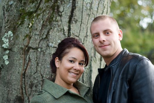 A young happy couple outdoor by a tree on a fall day.