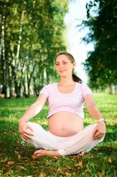 Beautiful pregnant woman relaxing on the grass in the park