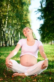 Beautiful pregnant woman relaxing on the grass in the park