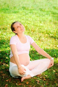 Beautiful pregnant woman relaxing on the grass in the park