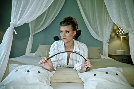 beautifull provocativ young woman lying on romantic bed with riding whip in her hand looking at the camera