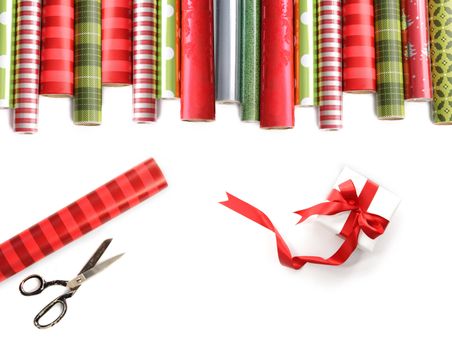 Rolls of colored wrapping  paper with scissors and gift on white background