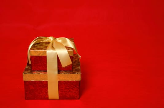 A wrapped gift box tied with gold satin ribbon on a red background.  Space for copy
