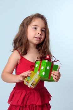 Young preschool girl holding presents.  She is wearing a red dress.