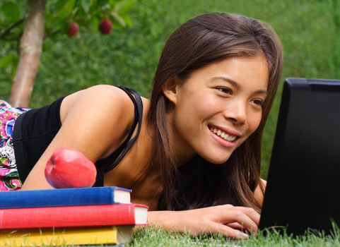 Student with laptop smiling while chatting / checking email in the park. Beautiful mixed race caucasian / asian model.