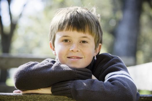 Portrait of a Cute Young Boy Leaning on a Wooden Railing Smiling Directly To Camera
