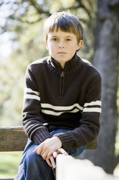 Portrait of a Cute Young Boy Sitting on a Wooden Railing Looking Directly To Camera