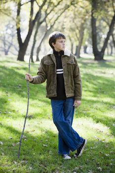Young Boy Standing With Stick in a Park Looking Away From Camera