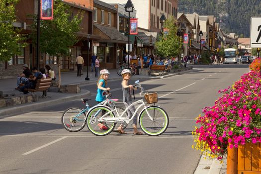 Two young girls crossing the streets of the town of Banff with their bicycles