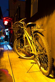 Old bicycle against wooden wall under amber light at night in a quiet street