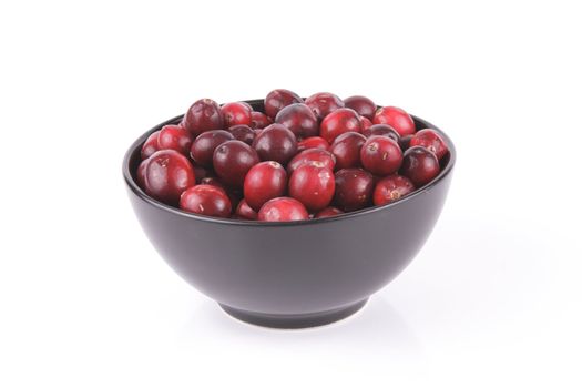 Red ripe cranberries in a small round black bowl with a reflective white background