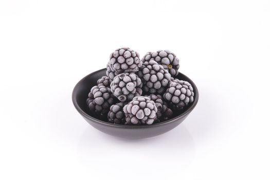 Black ripe frozen blackberries in a small round black dish with a reflective white background