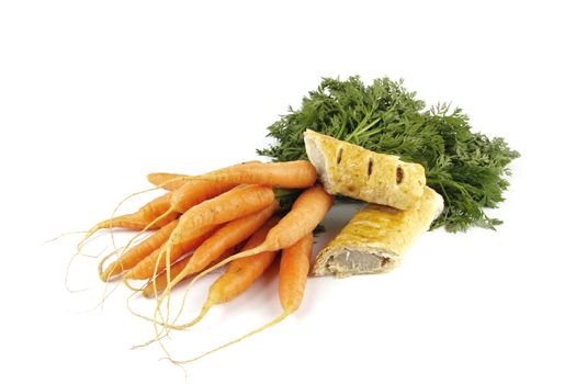 Contradiction between healthy food and junk food using bunch of carrots and sausage roll on a reflective white background 