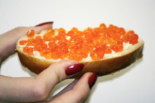 The female hand holds a sandwich with oil and red caviar. It is a delicacy.