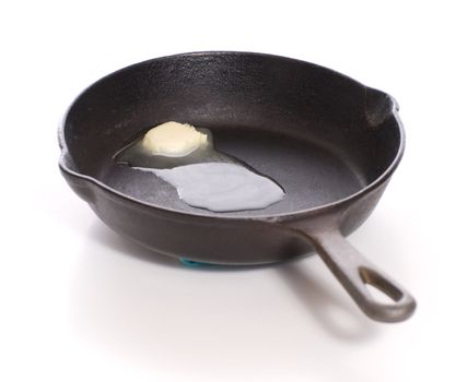 A cast iron pan with some butter melting in the bottom of it, shot on white