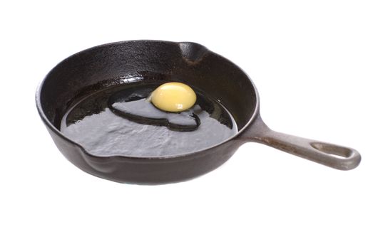 A black cast iron pan with a fresh chicken egg about to be fried, isolated against a white background