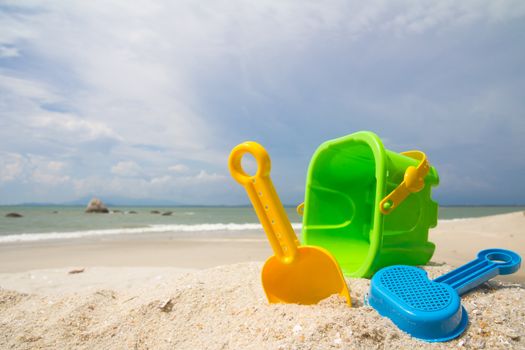 Child's bucket, spade and other toys on tropical beach against blue sky