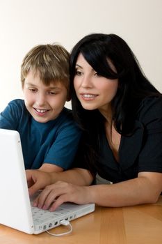 A woman using a computer while a child happily, ooks on.