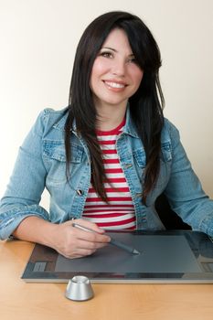 A smiling woman sitting at desk using a graphic tablet