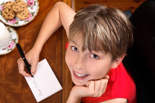 A child sitting at a desk writing a letter for Santa or Christmas card.