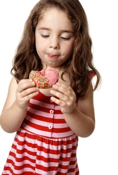 Young girl eating a delicious pink iced doughnut.  She is looking down at it  and licking her lips.