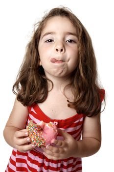 A little girl in a red striped dress is  holding a pink iced doughnut and licking her lips with satisfaction.