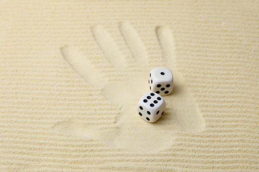 Print of a palm on sand with dices
