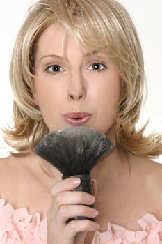 A female blowing gently to remove excess loose powder from a brush.