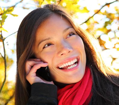 Happy woman on the mobile phone outside in park. Beautiful mixed race caucasian / asian woman,