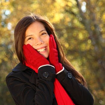 Happy autumn woman holding her head smiling being happy and surprised in forest in the fall. Very beautiful mixed caucasian / asian model.