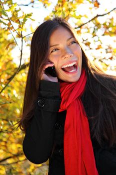 Happy laughing young woman on cell phone outside in park. Beautiful mixed race caucasian / asian woman,