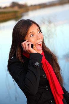 Happy excited woman on cellphone outside by waterside. Beautiful mixed race caucasian / asian woman,