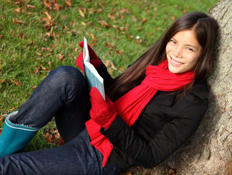  Reading book and relaxing outdoors in park under tree in autumn.