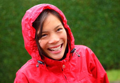 Rain woman. Beautiful young woman in red rain coat smiling having fun outside while it is raining heavily.