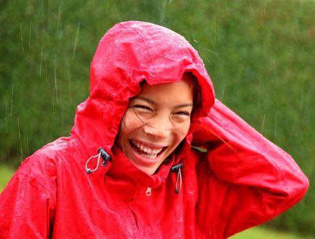 Rain woman. Beautiful young woman in red rain coat laughing having fun outside while it is raining heavily.