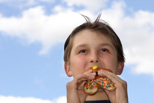 A boy biting into a donut against a blue sky