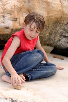 A casually dressed boy amuses himself playing with stones among sandstone rocks outdoors