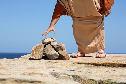 Closeup of a man dressed in anicent clothing standing by a pile of stones bending over to pick one up - concept  stoning, sin, punishment,  Stoning was used in many ancient cultures for crimes. Stoning of animals was also carried out if that animal killled a person. Stoning is still allowed in Iran, Nigeria, Afganistan, Pakistan.