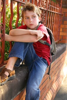 Child sitting on the edge of a brick and wrought iron wall.