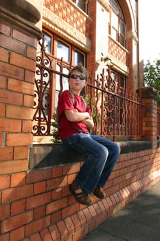 Child sitting on brick wall outside a school building.