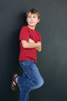 Young casually dressed boy leaning against a dark wall.